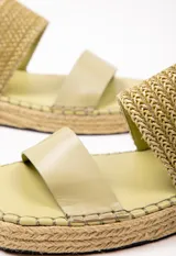 Sandalia con doble tira en el empeine, una de cuero color tostado y otra tejida en rafia. Plataforma de yute de 3.5 cm de alto.