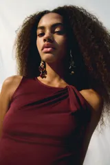 Top sin mangas color vino tinto, de tejido elástico y ajuste entallado, con un nudo drapeado en el hombro que crea un escote asimétrico.