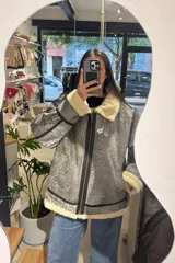 Campera bomber oversize de cuero gris con efecto gastado, forrería y detalles de corderito sintético color marfil en cuello, puños y ruedo. Cuenta con cierre frontal y costuras reforzadas.