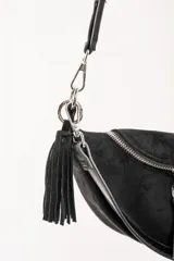 Cartera tipo bandolera de tamaño pequeño, confeccionada en material sintético con textura de gamuza en color marrón topo. Presenta un diseño semicircular con cierre superior, herrajes metálicos plateados y una correa larga ajustable de cinta técnica.