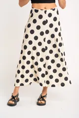 Falda midi color crudo con estampado de lunares negros, corte evasé y cintura alta.