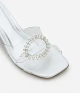 Sandalia mule con puntera cuadrada, capellada de vinilo transparente con aplique de pedrería plateada y tacón bloque plateado.