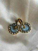 Aros de acero quirúrgico con dije circular de resina rosa y borde de strass dorados.