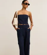 Pantalón recto de cintura baja, confeccionado en punto roma con rayas verticales en hilo teñido. Presenta trabillas en la cintura, cierre tradicional, pliegues, bolsillos cargo laterales y bolsillos falsos atrás.