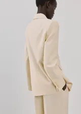 Blazer de diseño recto y estilo sastrero, color beige, confeccionado en mezcla de lyocell y poliéster. Cuenta con cuello en pico con solapas de muesca, manga larga, bolsillos delanteros con solapa y cierre frontal de un botón.