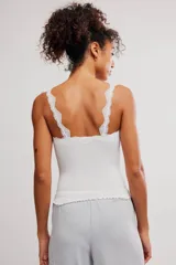 Musculosa blanca de tejido acanalado con detalles de encaje festoneado en el escote y los tirantes, corte ajustado y ruedo con terminación ondulada.