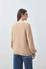 Cardigan de textura suave y efecto fluffy, color beige, con cuello redondo, cierre frontal con botones y puños acanalados.