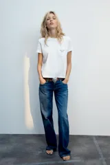 Camiseta blanca de algodón con cuello redondo, manga corta y bolsillo en el pecho que incluye un texto impreso a contraste.