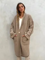 Sacón de lana color crudo, de punto acanalado, con cuello tipo chal, un botón frontal dorado y dos bolsillos delanteros.