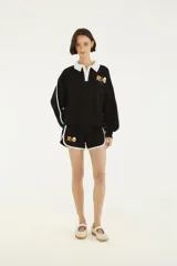 Short deportivo negro con ribetes blancos en los bordes y las aberturas laterales, con cordón ajustable en la cintura y estampa con la palabra "RIO" y un huevo frito en la pierna derecha.
