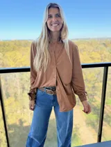 Camisa de manga larga confeccionada en tela simil gamuza, color marrón tostado, con cuello clásico y cierre frontal de botones.