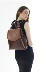 Mochila de cuero vacuno marrón con acabado pulido, solapa en forma de V y costuras decorativas. Cuenta con cremalleras laterales y asas ajustables.