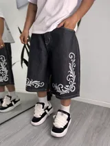 Bermuda baggy de denim negro con diseño holgado, tiro medio y pespuntes en contraste. Presenta un estampado blanco de estilo barroco en la parte inferior de las piernas.