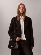 Cartera mediana con solapa Calvin Klein de color negro, confeccionada en poliuretano. Presenta diseño estructurado con cierre de broche a presión metálico dorado y correa ajustable.