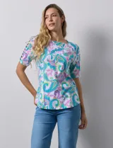 Remera de algodón estampado con diseño paisley en tonos celeste, rosa y amarillo. Tiene cuello redondo y mangas cortas con detalle de entrelazado y aberturas en los hombros.