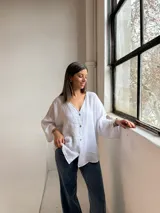 Camisa blanca de lino, con cuello en V, cierre frontal de botones y mangas amplias de corte holgado.