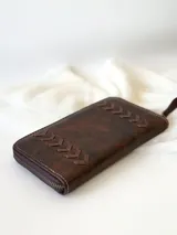 Billetera grande de cuero color marrón con cierre metálico y detalle de costuras en forma de espiga. Incluye monedero interno y espacio para billetes extendidos.