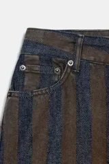 Jeans de tiro medio con corte barrel leg, confeccionados en denim con rayas verticales a contraste en tonos azul oscuro y marrón/tostado. Presentan cinco bolsillos y cierre frontal con cremallera y botón.