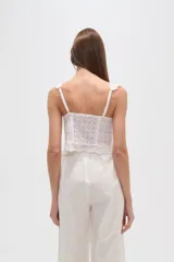 Top blanco de algodón con bordado broderie, corte ajustado al cuerpo, breteles finos y escote redondo. Presenta un cierre frontal con botones y elástico en la base.