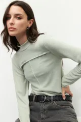 Polera blanca de manga larga con cuello alto y costuras cruzadas a la vista en el frente.