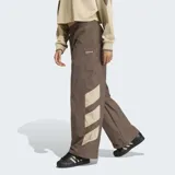 Pantalón deportivo Adidas de corte holgado, color marrón con detalles en beige en la parte inferior de las piernas. Presenta cintura elástica con cordón de ajuste y logo de la marca bordado en el muslo.