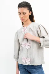 Blusa a rayas verticales grises y blancas con mangas abullonadas y tres lazos rosas en el frente.