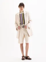 Saco sastrero estructurado confeccionado en sarga color beige, de largo por debajo de los muslos. Cuenta con cuello sastrero con solapa de pico ancha, broches dorados, hombreras, bolsillos con tapa y detalles en tela complemento en el cuello y bolsillos.