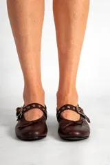 Chatas de cuero color chocolate, con punta redondeada, tira sobre el empeine con hebilla plateada y pequeño moño decorativo en la punta.