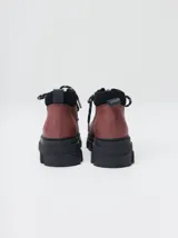 Bota acordonada de estilo montañés con suela track de goma robusta. Confeccionada en cuero con detalles de gamuza en la talonera y tirador trasero. Presenta costuras a contratono y cordones bicolores.