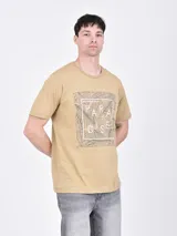 Remera de manga corta color beige con cuello redondo y un estampado gráfico central que incluye hojas tropicales y la palabra "Paradise".