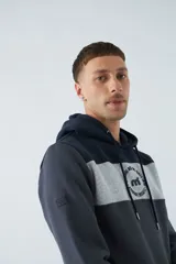 Buzo canguro de felpa color borgoña, con capucha ajustable con cordones color beige, bolsillo tipo canguro y logo estampado en el pecho. Tiene una franja horizontal blanca en el pecho y puños y cintura acanalados.