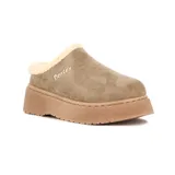 Pantuflas tipo sueco de gamuza color taupe, con interior forrado en corderito sintético color crema y plataforma de goma al tono. Presenta el logo de la marca bordado en el lateral.