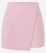 Short pollera de sastrería color rosado, con diseño asimétrico superpuesto en el frente, bolsillos ribeteados decorativos y cierre lateral discreto.