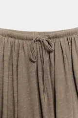 Falda midi de corte acampanado, confeccionada en tejido de algodón con textura flamé. Presenta cintura elástica con cordón ajustable y diseño fluido con godets.