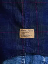 Camisa de pana color azul marino, con mangas largas, cuello clásico y dos bolsillos frontales con solapa y botón.