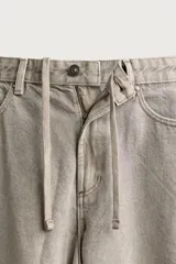 Pantalón barrel fit de mezclilla color verde militar, con efecto lavado, cinco bolsillos, cierre frontal con cremallera y botón, y detalle de pinzas en las rodillas.