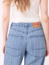 Jean de corte wide leg con diseño de rayas verticales finas en tono azul claro. Presenta cierre frontal con botón y bolsillos laterales.