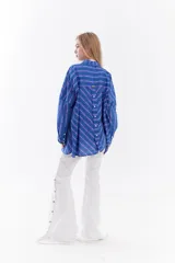 Camisa oversize de algodón con estampado de rayas multicolor en distintas direcciones, cuello camisero, mangas largas y detalle de botonera vertical en la espalda.