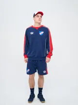 Buzo deportivo azul marino con detalles en rojo y blanco en cuello, hombros y mangas, de cuello redondo y manga larga, con el logo de Umbro y el escudo del Club Nacional de Football bordados en el pecho.