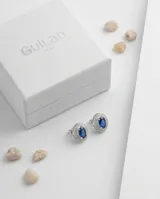 Caravanas de plata 925 con diseño ovalado, piedra central azul tipo zafiro rodeada por un marco de circonias brillantes.