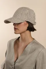 Gorra con visera confeccionada en lana fina sin teñir, con diseño de estampado tipo pata de gallo en tonos beige y blanco.