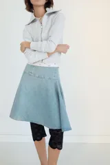 Falda midi de denim en tono azul claro, con tiro medio y diseño asimétrico con tablas laterales. Cuenta con cierre lateral mediante cremallera metálica.
