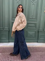 Pantalón tipo jean cargo de corte ancho y tiro alto, confeccionado en denim azul oscuro. Presenta bolsillos laterales tipo cargo con solapa y costuras reforzadas a lo largo de las piernas.