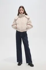 Campera puffer de color beige con cuello alto, capucha desmontable, cierre frontal y bolsillos laterales. Diseño de corte holgado con puños elásticos.
