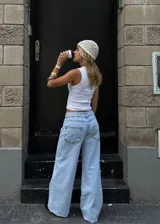 Pantalón de jean estilo wide leg, tiro bajo, con diseño de cinco bolsillos y cierre frontal con botón y cremallera. Presenta un lavado claro y corte holgado en las piernas.