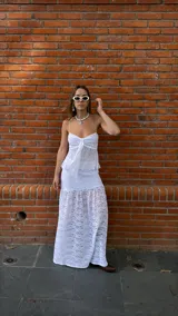 Pollera larga de encaje blanco con volados en el ruedo. Tiene un top a juego con breteles finos y volados en el busto, con un lazo en el centro.