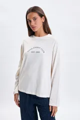 Remera de manga larga en color crudo con cuello redondo y estampa frontal con texto en azul marino.