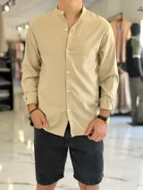 Camisa de lino color beige, de manga larga con puños arremangados y cuello mao. Cuenta con cierre frontal de botones y diseño clásico.