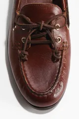 Zapatos náuticos de cuero marrón con cordones en el empeine, ojetes metálicos y costura tipo mocasín en la puntera.