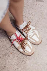 Zuecos de cuero color beige, con cordones marrones y verdes, y detalles de costuras.